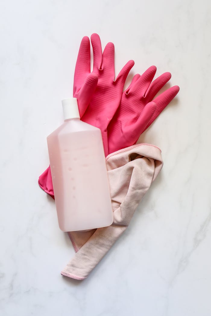 services-03 A flat lay of pink rubber gloves, a cleaning cloth, and a bottle on a white background for cleaning themes.