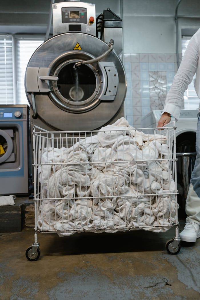 A worker handling a cart of white linens in an industrial laundry setting.